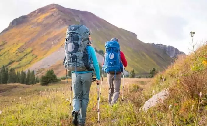 Two adults carring two backpacks while hiking