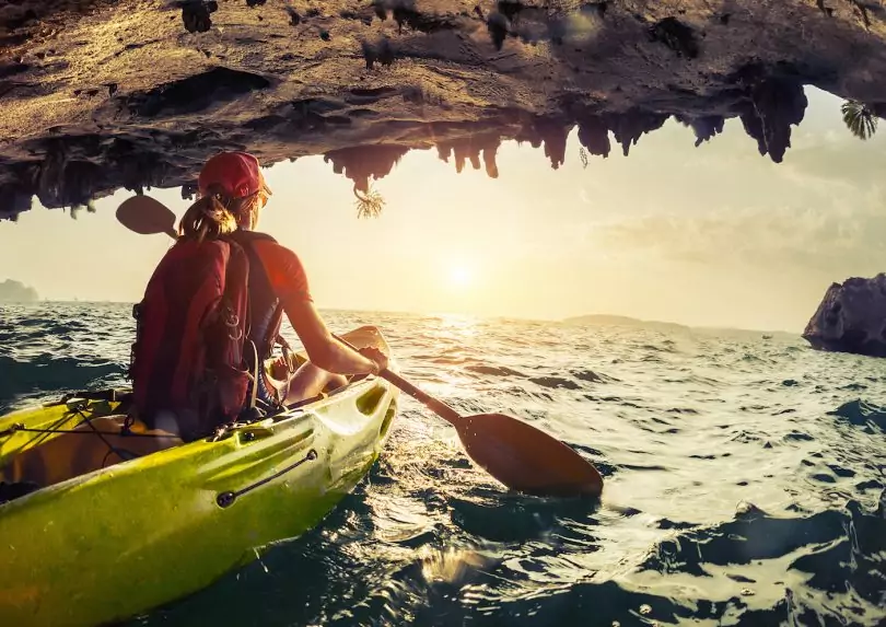 Lady paddling the kayak in the rough sea at sunset.