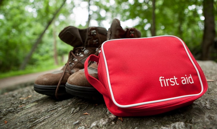 A red first aid kit with hiking boots in the woods.