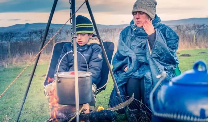 Woman wearing a poncho is near a camp fire next to her son