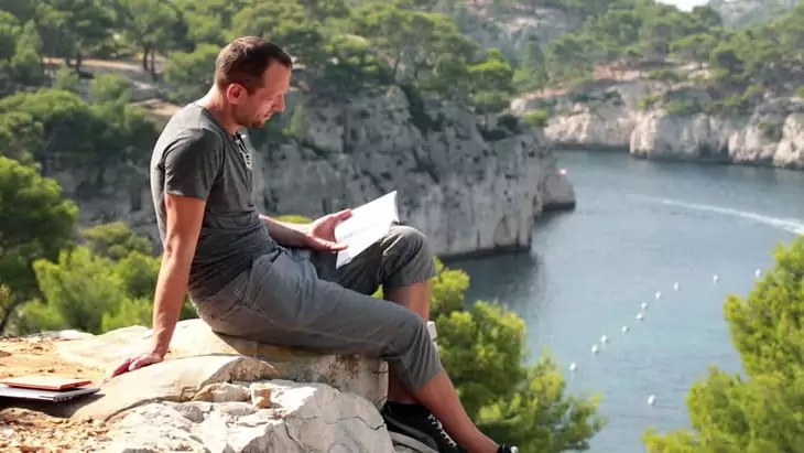 Man reading book on cliff in beautiful nature scenery