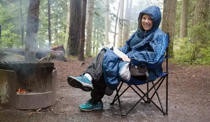 Woman near a camp fire is wearing a blue poncho