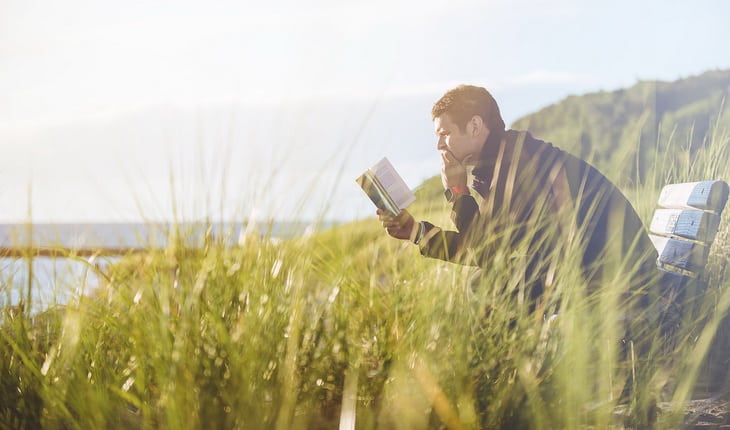 A man reading a book on a bench