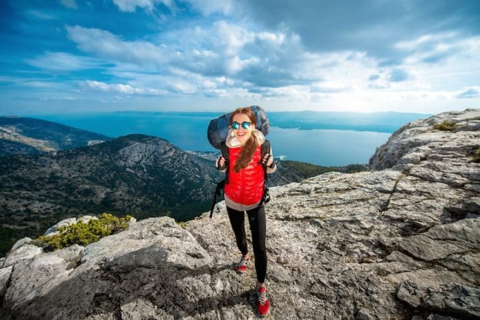 A woman with a backpack and wearing leggins is on top of the moutains