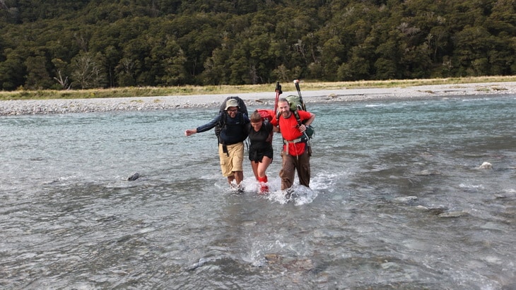 Three adults crossing a river