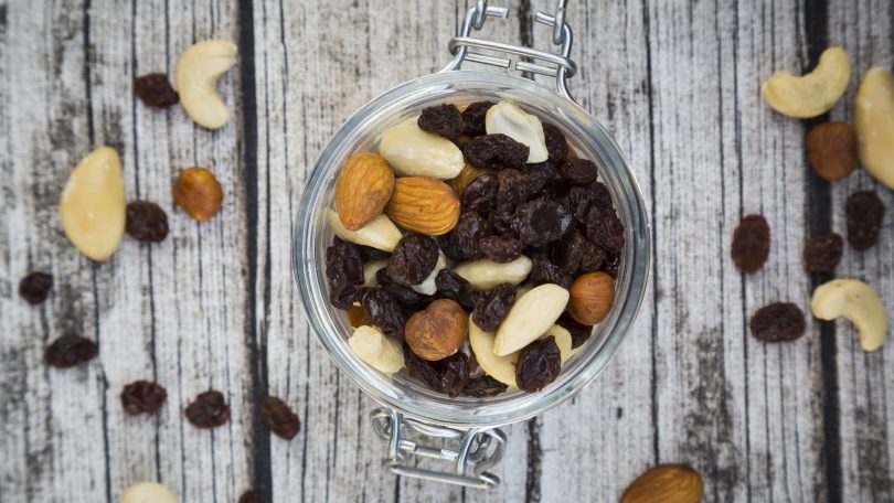 Mixed nuts and raisins in glass on wood