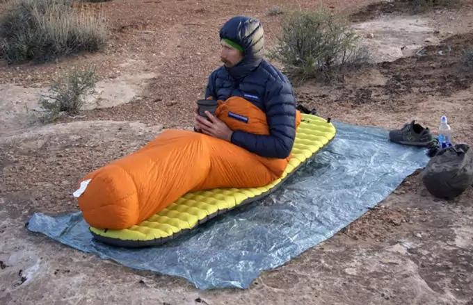 A man in a sleeping bag holding a cup of hot coffee