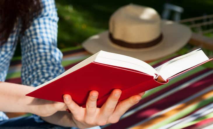person-reading-red-covered-book-near-grass