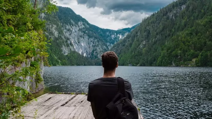 Man Carrying Black Backpack Standing on Brown Wooden Dock during Daytime