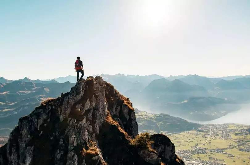 Man Standing on Brown Rocking Mountain Under Blue Sky and Yellow Sunlight