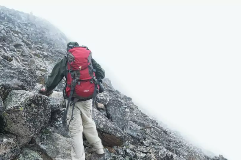 Man in Green Jacket With Red and Black Backpack Climbing Mountain