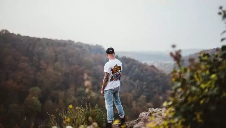 Man in White Printed Crew Neck Shirt Standing on Isle of Mountain