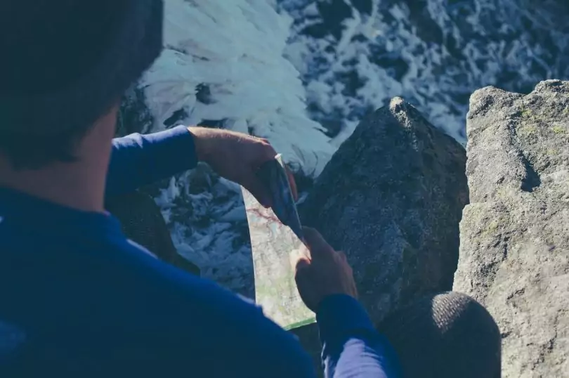 Man Sitting on Rock Near Body of Water and Holding a Map