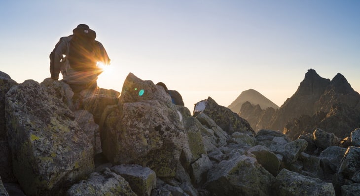 Person Sitting on Gray Rocks Under Clear Blue Sky