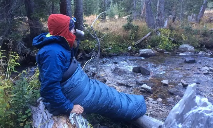 Man in a sleeping bag sitting and watching the nature around him