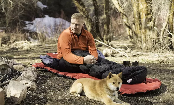 Man in Klymit KSB 20 Sleeping Bag and a dog next to him