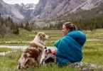 Woman in sleeping bag sitting on the grass and looking at her dog