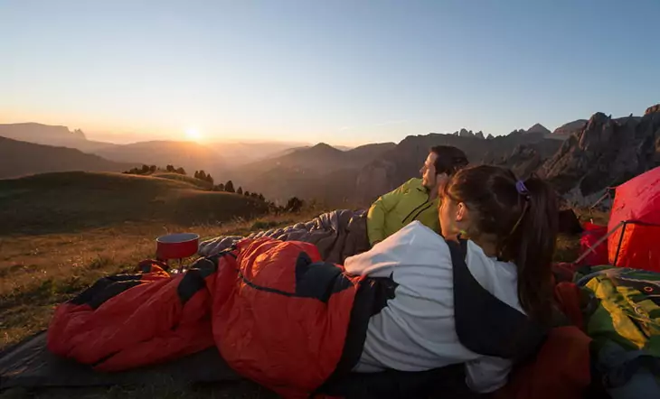 Two people laying in sleeping bags watching the sunrise