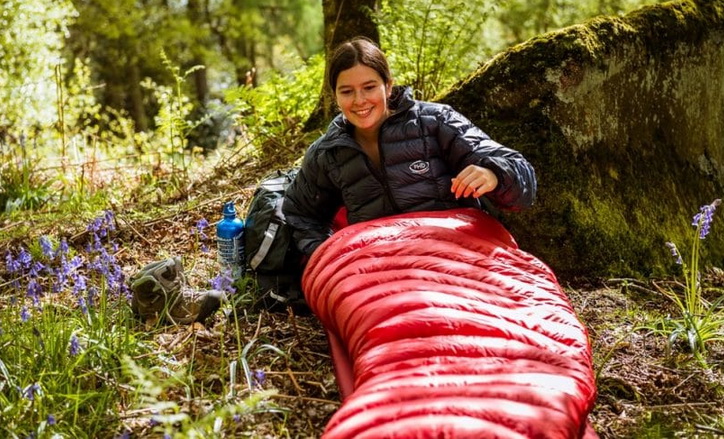 woman in a sleeping bag sitting on the grass in the wild