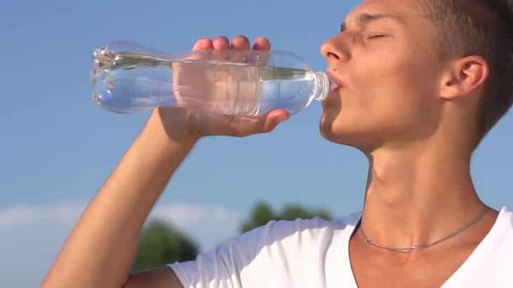 Healthy Young Man Drinking Water from the bottle outdoors.