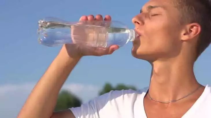 Healthy Young Man Drinking Water from the bottle outdoors.