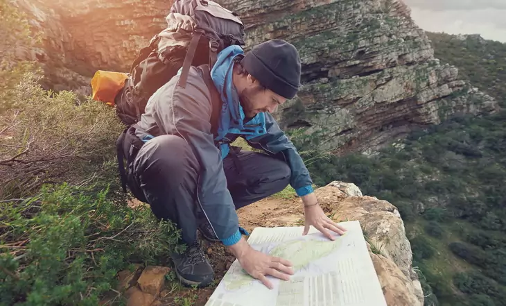 Lost hiker with backpack checks map to find directions in wilderness area