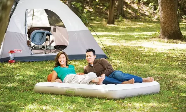 Two adults sitting outside on the most comfortable camping bed