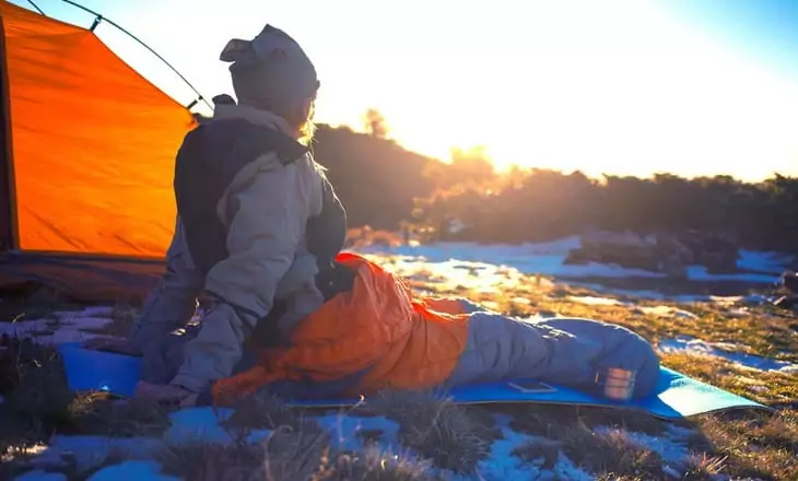 Girl sitting in a sleeping bag and watching the landscape in the morning