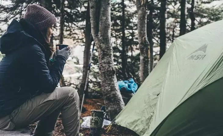 Woman near a tent driking hot coffee in the morning