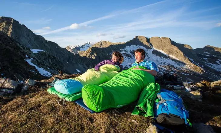 Two adults sitting in sleeping bags outside in the nature