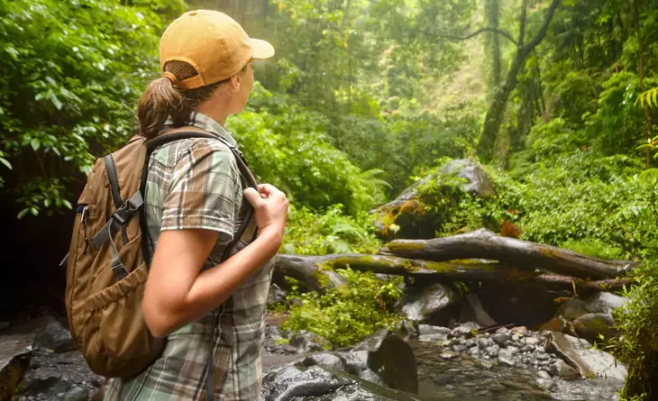 Young backpacker with backpack traveling along rain forest.Tourist hiking in the deep jungle