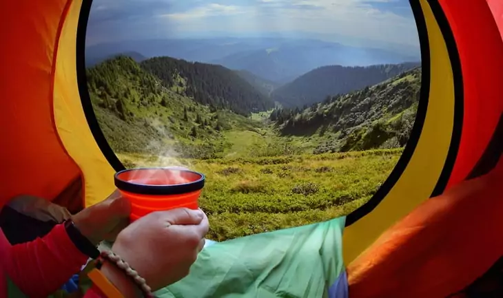 Woman lying in a tent with coffee ,view of mountains and sky in Carpathians mountains, Ukraine,