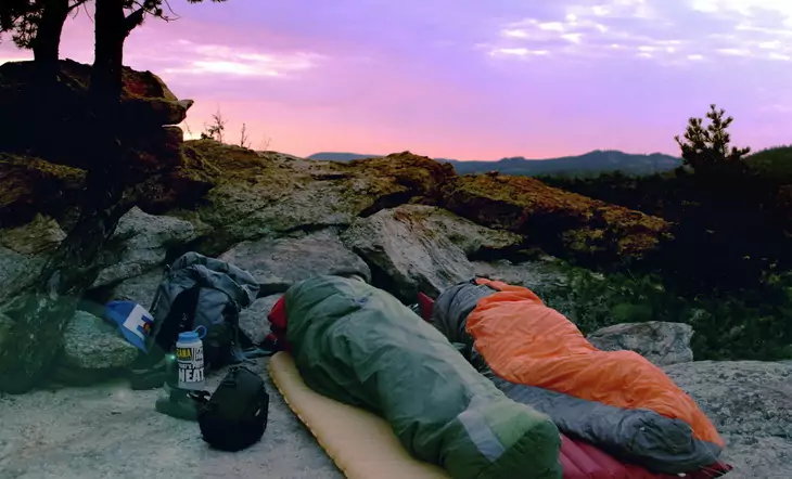 Two people in sleeping bags sleeping outside in the wild