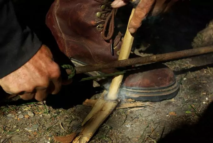 A man starting a fire with a bow drill