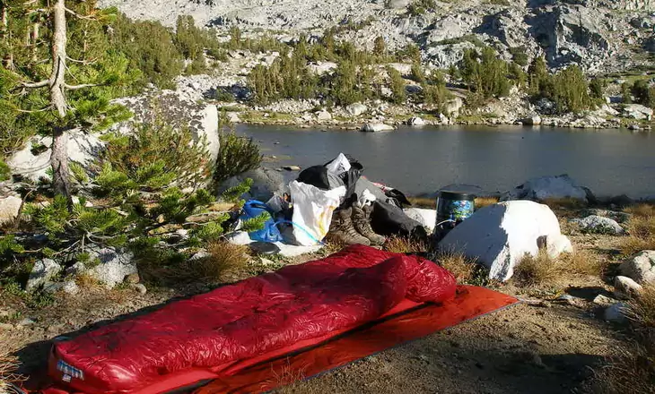 Western Mountaineering sleeping bag on the ground outside near a water and mountains