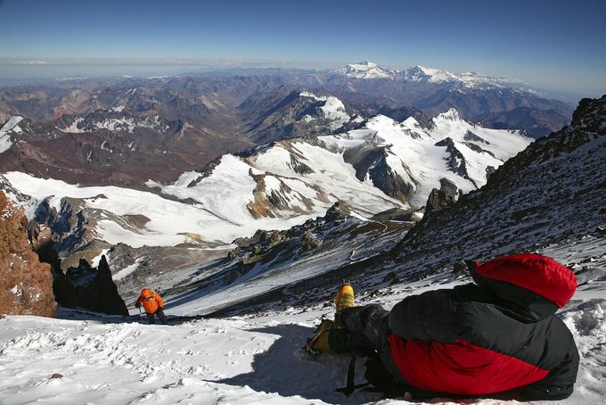 An exhausted climber rests and waits for a team member on summit