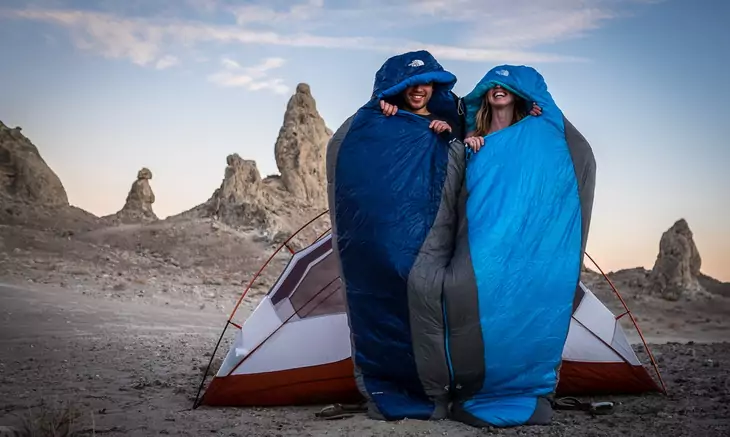 Two aduls in The North Face Cat's Meow Sleeping Bag near a tent outside