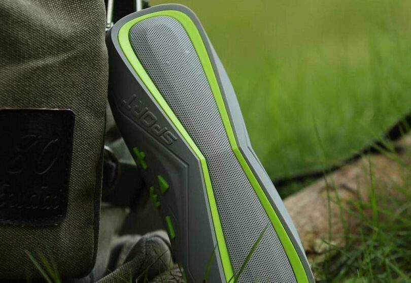 Sport silver-green wireless bluetooth speaker and a backpack on the grass