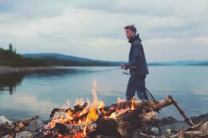 Man fishing outside the tent and fire burning