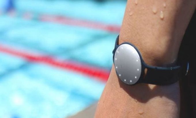 Waterproof fitness tracker worn on left hand by a person standing next to a swimming pool