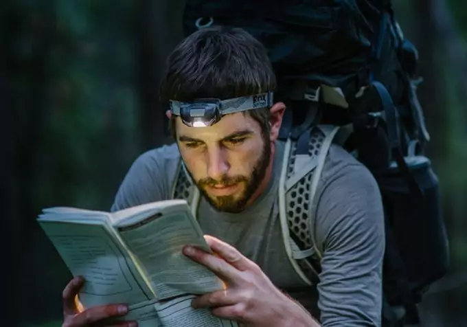 backpacker with headlamp reading a map